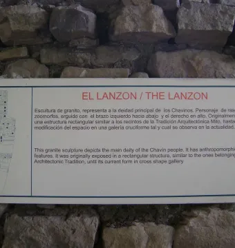 Informational sign about the Lanzón mounted on a rough stone wall, with a line drawing of the carved figure.