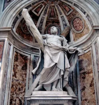 Stone statue of Saint Andrew in a decorated marble alcove, with one arm raised to a wooden beam behind him.