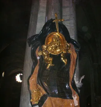 Memorial to Maria Raggi with gilded medallion, putti, and cross on a marble monument in a dim church interior.