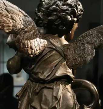 Back view of Putto with a Dolphin bronze sculpture, showing the winged figure, curled hair, drapery, and the dolphin’s tail.
