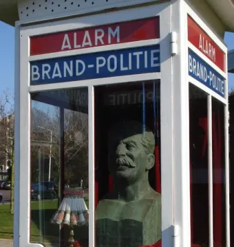 Stalin Bust and Herring sculpture inside a white-framed glass enclosure with emergency signage, with a small lamp beside it.