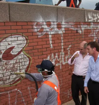 Workers clean graffiti from the Monument to General Carlos M. de Alvear while two men observe nearby.