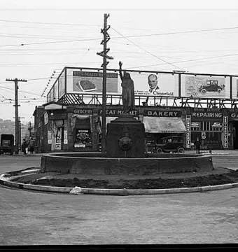 Chief Seattle statue with a raised arm on an ornate pedestal in a circular street island.