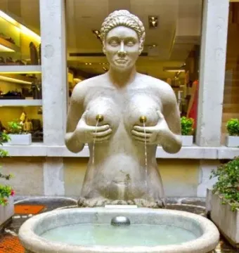 Fontana delle Tette stone fountain with a topless female statue and water flowing into a round basin.