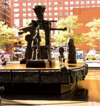 La Joute bronze fountain sculpture with abstract figures and water at its base in an urban plaza.