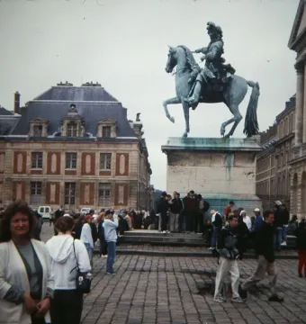 The Equestrian Statue of Louis XIV on a tall stone pedestal overlooking a crowded square at Versailles.