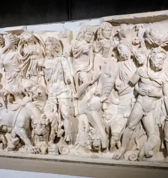 White marble sarcophagus with a densely carved triumphal procession of draped figures and animals in high relief.