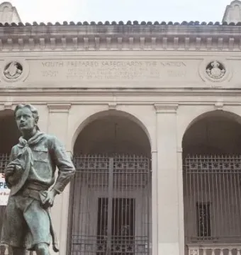 The Ideal Scout sculpture stands in front of a stone building with arched entryways and carved details.