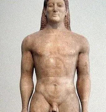Kroisos Kouros, a front-facing ancient marble statue of a nude young man with braided hair, standing with one leg forward.