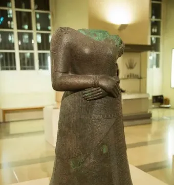 Headless statue of Napir-Asu with hands clasped at the waist and an intricately decorated long garment.