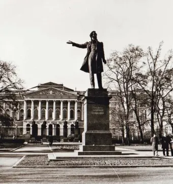 Pushkin statue on a tall pedestal in front of a columned building with trees nearby.