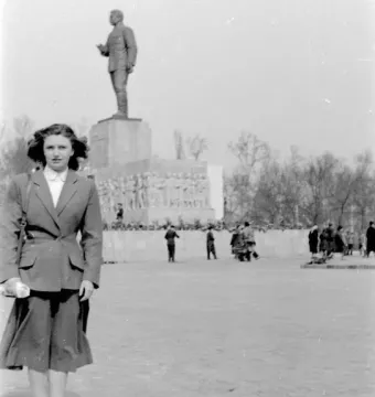 The Stalin Monument rises on a tall pedestal in a large square, with a woman posing in the foreground and people nearby.