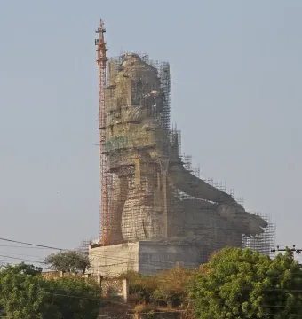 Statue of Belief under construction, draped in scaffolding and protective netting with a crane beside it.