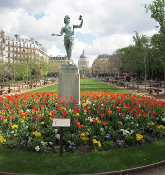 The Greek Actor sculpture on a tall stone pedestal in a flower bed of red and yellow tulips in a Paris park.