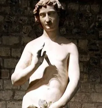 Adam statue with curly hair, one hand raised and the other holding leaves over his lower body.