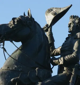 Andrew Jackson equestrian statue in bronze, showing Jackson raising his hat beside the horse’s head against a blue sky.