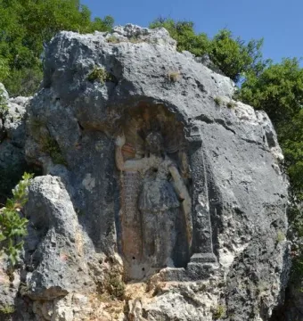 Athena relief carved into a rock face, with a robed figure, a standing column, and carved inscriptions beside it.