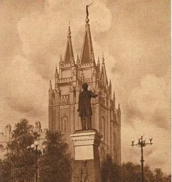 Brigham Young Monument on an ornate pedestal with a figure standing atop and pioneer figures below, with a grand spired building in the background.