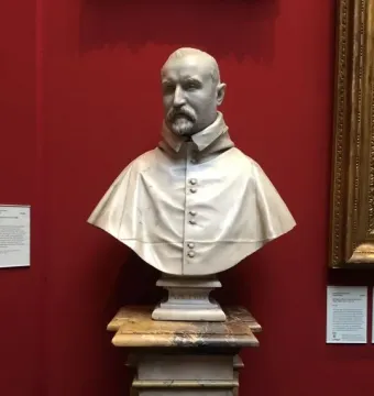Bust of Carlo Antonio del Pozzo in white marble on a tiered pedestal against a red wall.