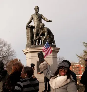 The Emancipation Memorial with Abraham Lincoln standing over a kneeling enslaved man on a stone pedestal, with people gathered around it.