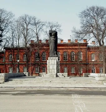 Karl Marx Monument standing in front of a long red brick building with arched windows.