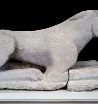 Leona de Baena stone sculpture of a crouching feline beast with its jaws open, displayed on a white base.