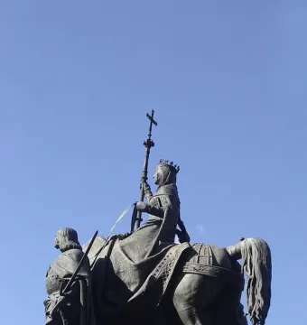 The Monument to Isabella of Castile, a dark bronze equestrian statue of a crowned woman holding a cross-topped staff beside a soldier figure.