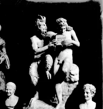 Pan and Daphne marble sculpture showing a bearded, horned figure embracing a nude youth holding a small musical instrument.