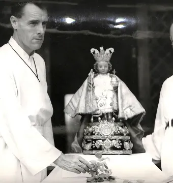 Santo Niño de Cebú statue on an ornate pedestal, flanked by two men in clerical attire.