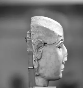 Side profile of the Warka Mask on a dark display stand.