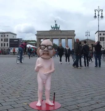 Citizen Włapko sculpture on a red circular base in a square, with the Brandenburg Gate in the background.
