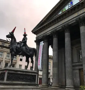Duke of Wellington equestrian statue with red and white traffic cones on the rider and horse heads, in front of a columned gallery building.