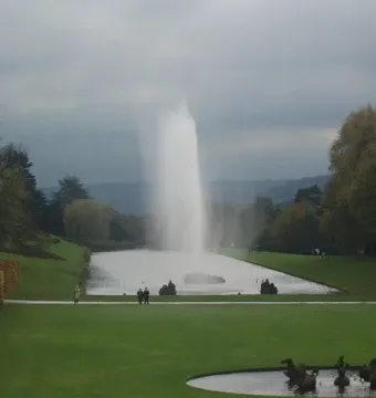 The Emperor Fountain sends a tall plume of water over a long lake at Chatsworth, framed by lawns, hedges, and autumn trees.