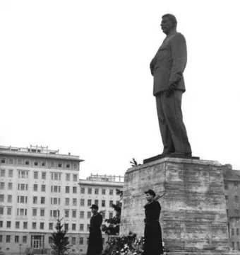 Statue of Joseph Stalin on a stone pedestal, flanked by two armed guards and decorated with flowers.