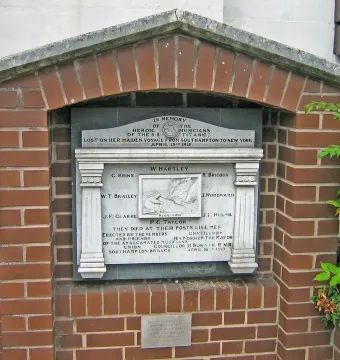 Titanic Musicians\' Memorial plaque set in a red brick archway with carved inscriptions and a relief of a musician playing an instrument.