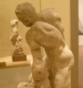 Two Wrestlers sculpture showing two nude male figures locked in a wrestling embrace on a dark base inside a display case.