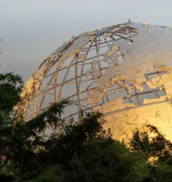 Unisphere partially visible through lush green foliage, with its metallic grid and continental shapes catching warm light.