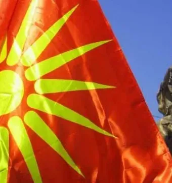 Bronze Warrior on Horseback statue partially visible beside a large red flag with a yellow sun emblem.