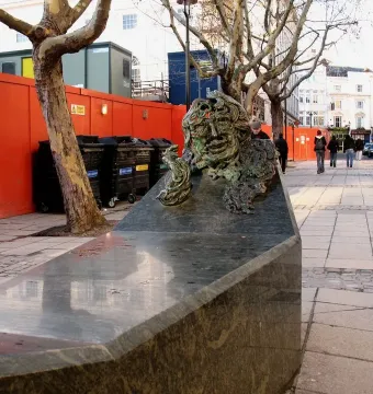 A Conversation with Oscar Wilde sculpture on a granite bench beside a paved walkway.
