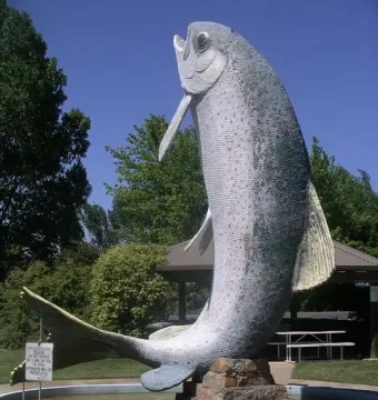 The Big Trout sculpture standing in a circular pool with trees and a gazebo nearby.