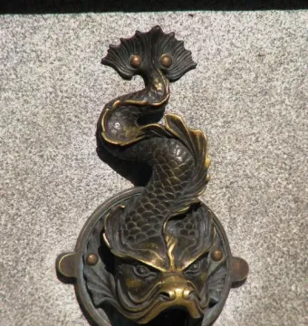 Bronze-colored dragon-shaped fountain spout on the Nicolaus Copernicus Monument, with water flowing from its mouth.