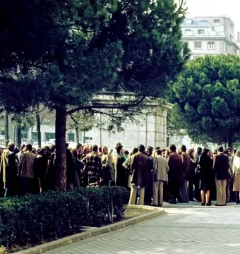 Stone plinth of the Equestrian Statue of Francisco Franco partly hidden by trees, with a crowd gathered around it.