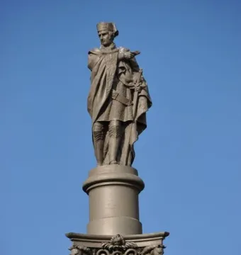 Galceran Marquet statue atop an ornate column, with a robed figure holding a sword against a blue sky.