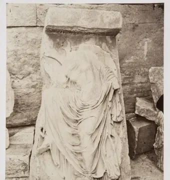 Weathered stone relief of Nike untying her sandal, shown in sepia tones.