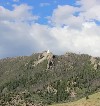 Our Lady of the Rockies statue standing on a rocky, tree-covered mountain summit