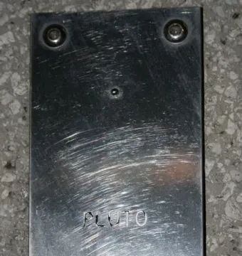Scratched silver Pluto plaque with a small planet sphere and scientific data.