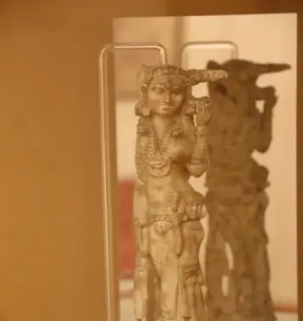 Pompeii Lakshmi ivory figurine shown on a clear stand with its reflection visible in a mirror behind it.