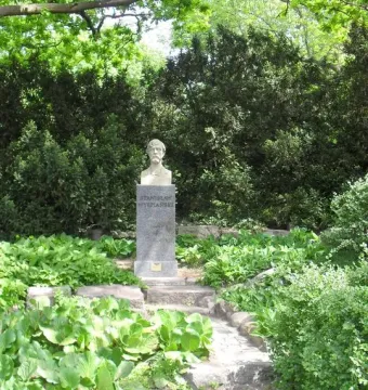 Bust of Stanisław Wyspiański on a tall stone pedestal in a garden