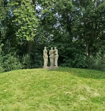 Three Standing Figures sculpture on a grassy knoll surrounded by dense green trees.