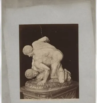 The Wrestlers marble sculpture showing two nude male figures in a wrestling pose on a dark base.
